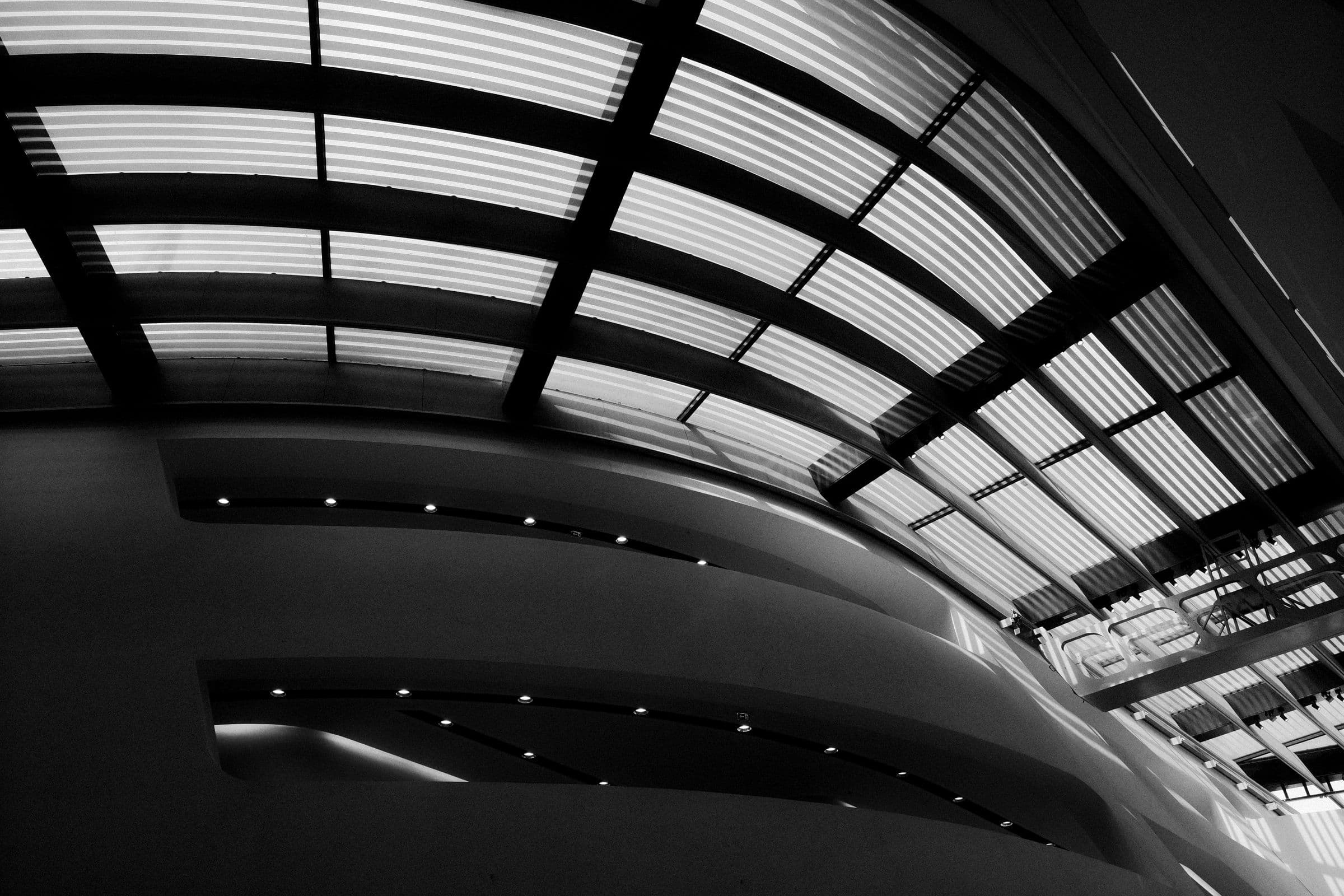The ribbed underside of a sweeping architectural roof, lit from its outer edge.