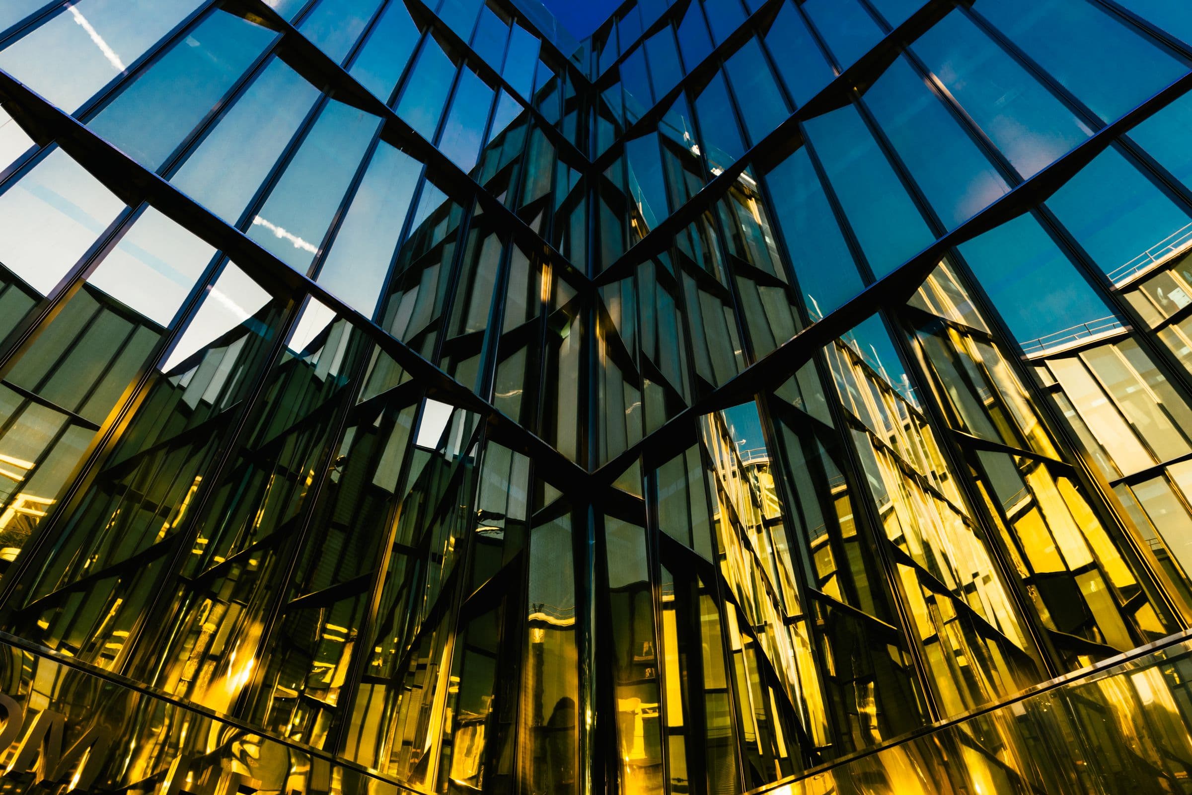 Angled glass panels on a building facade catching gold and deep blue light.