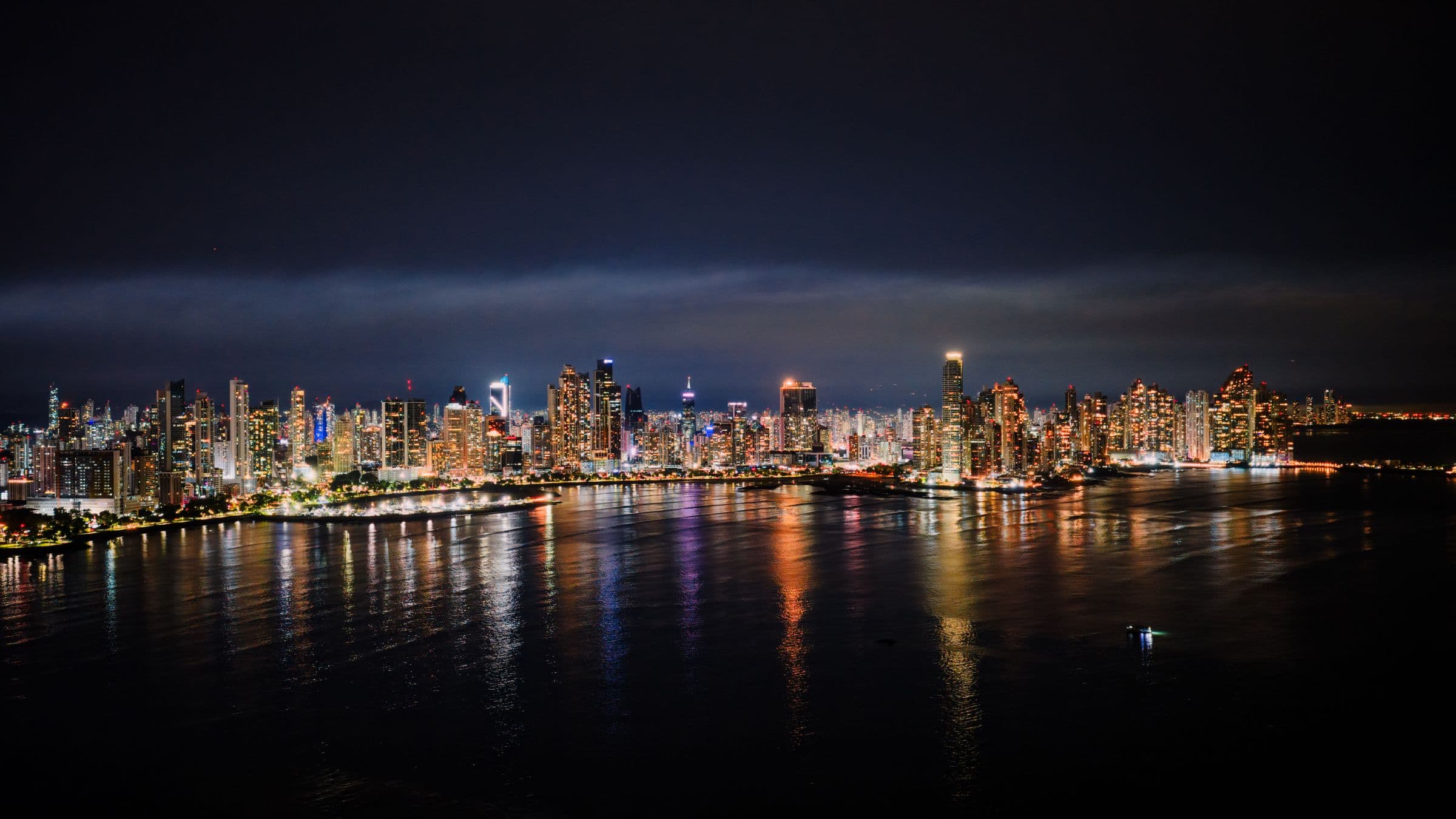 A waterfront city skyline at night reflected across still water.
