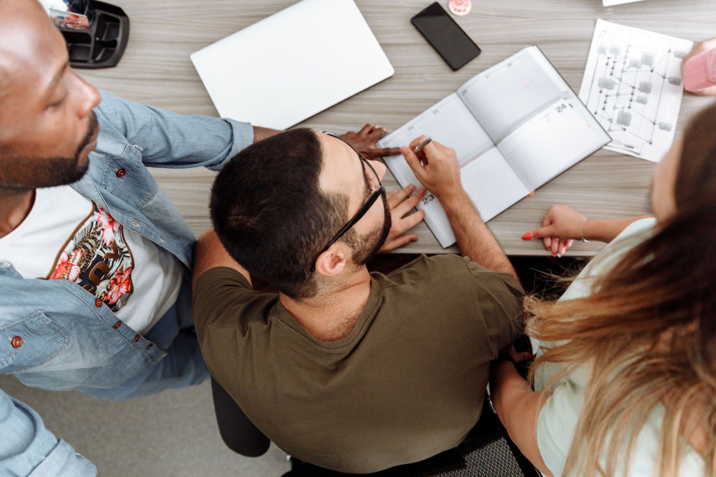 Overhead view of a team working across a shared table of notebooks and sketches.