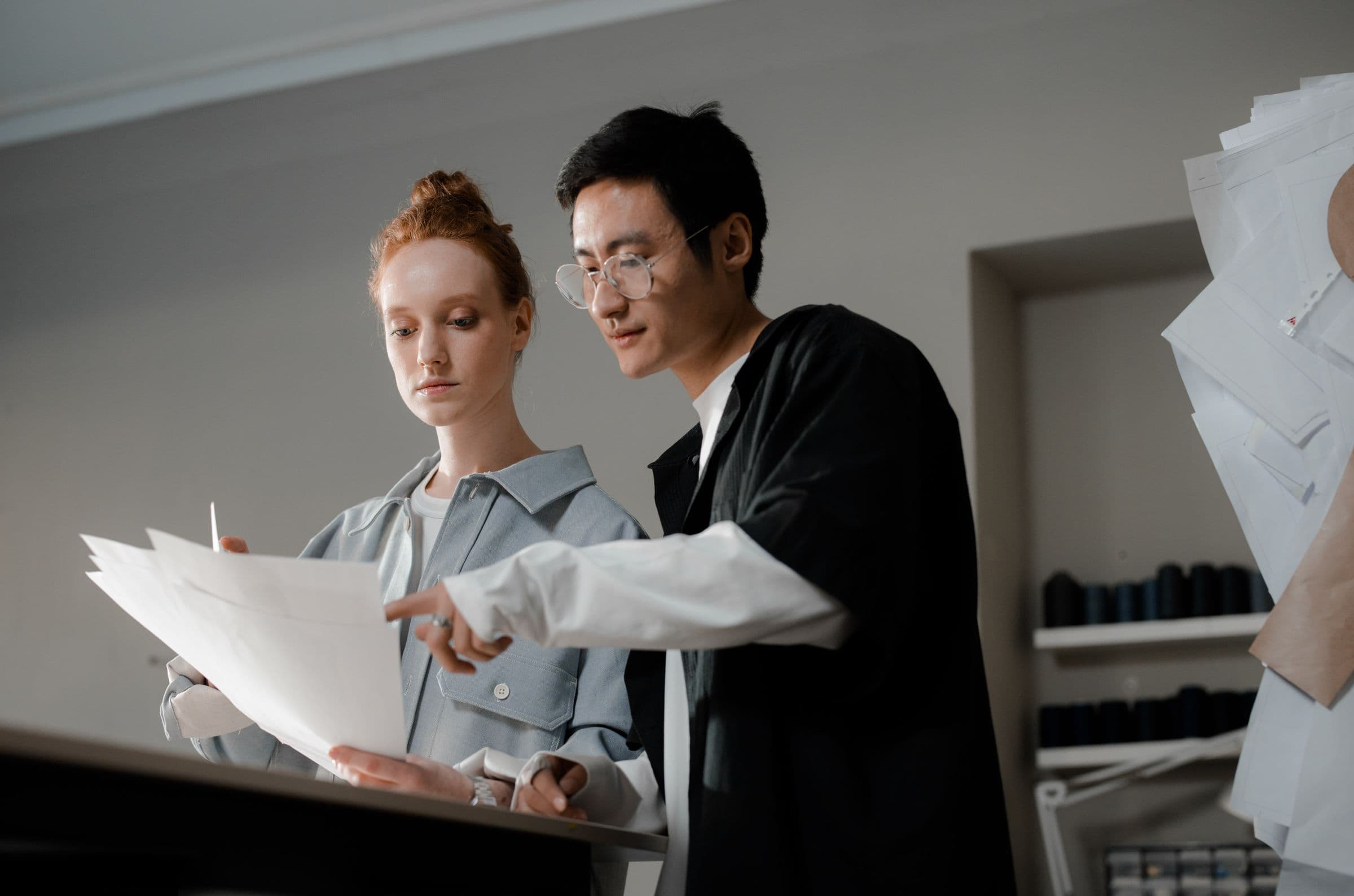 Two colleagues comparing printed sketches side by side in a bright studio.