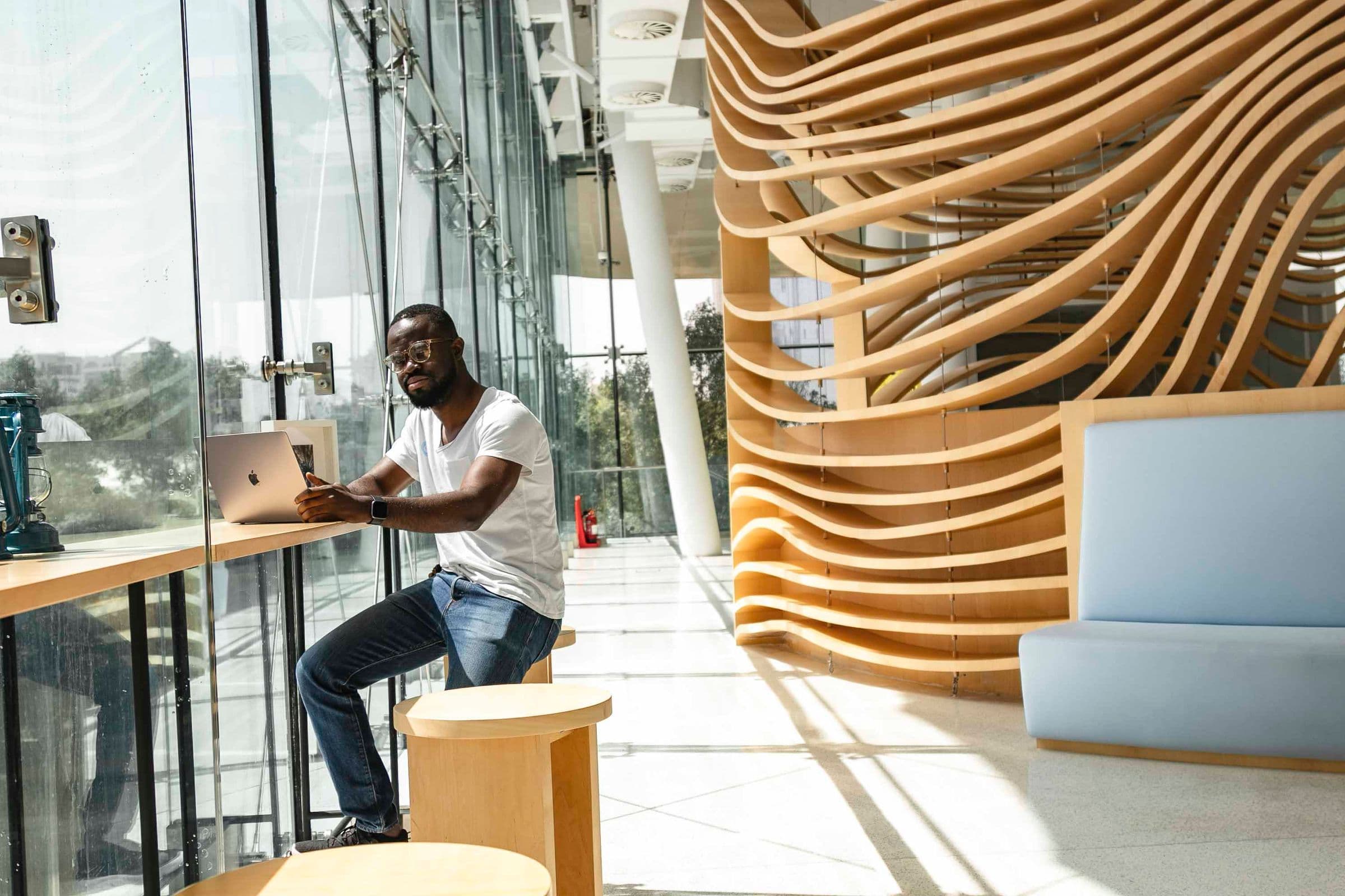 Someone working from a window seat beside a sculptural timber staircase.