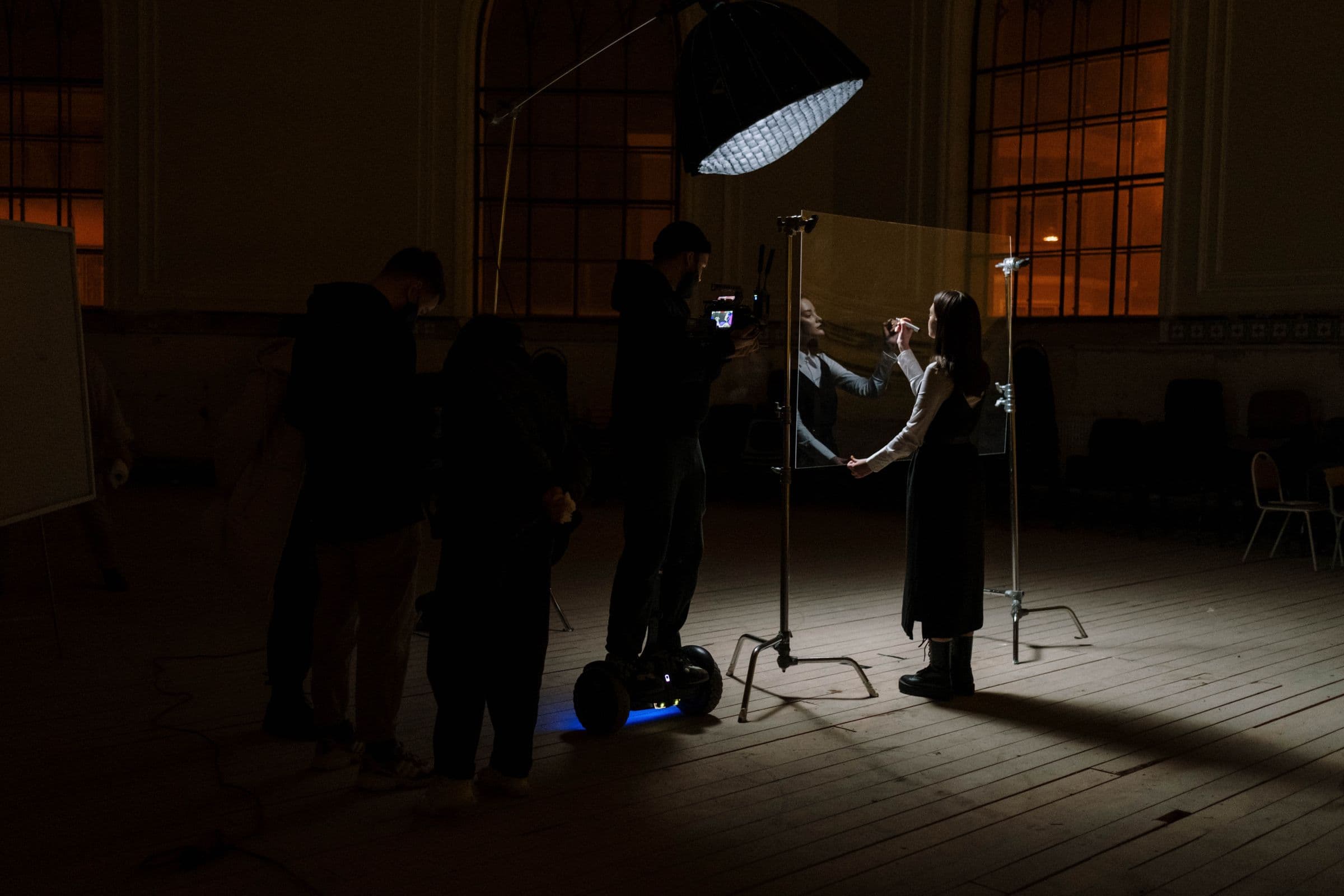 A film crew lighting a scene with a large softbox in a tall, dark hall.