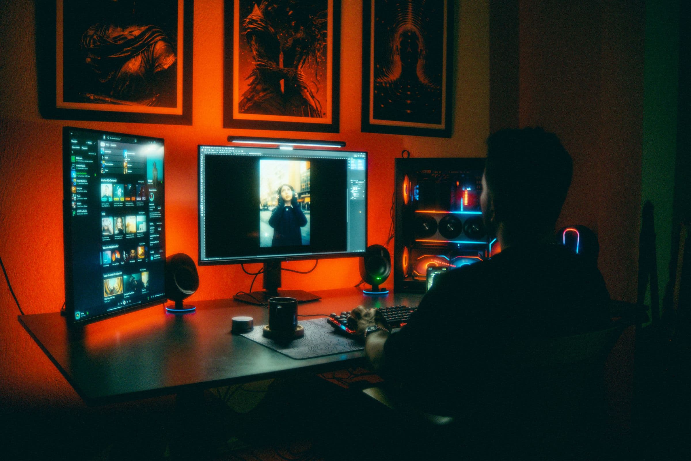 An editor at a multi-monitor suite lit by warm and cool practical lights.