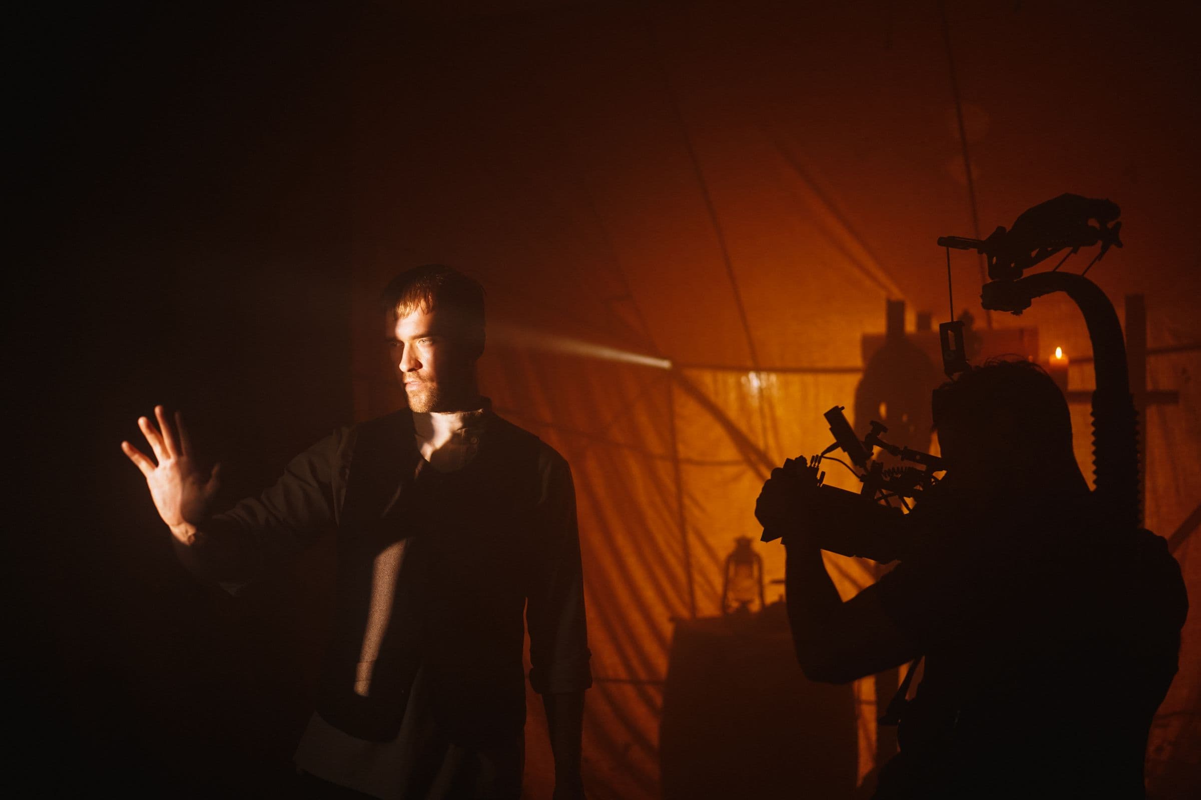 A performer lit against warm haze while a camera operator frames the shot.