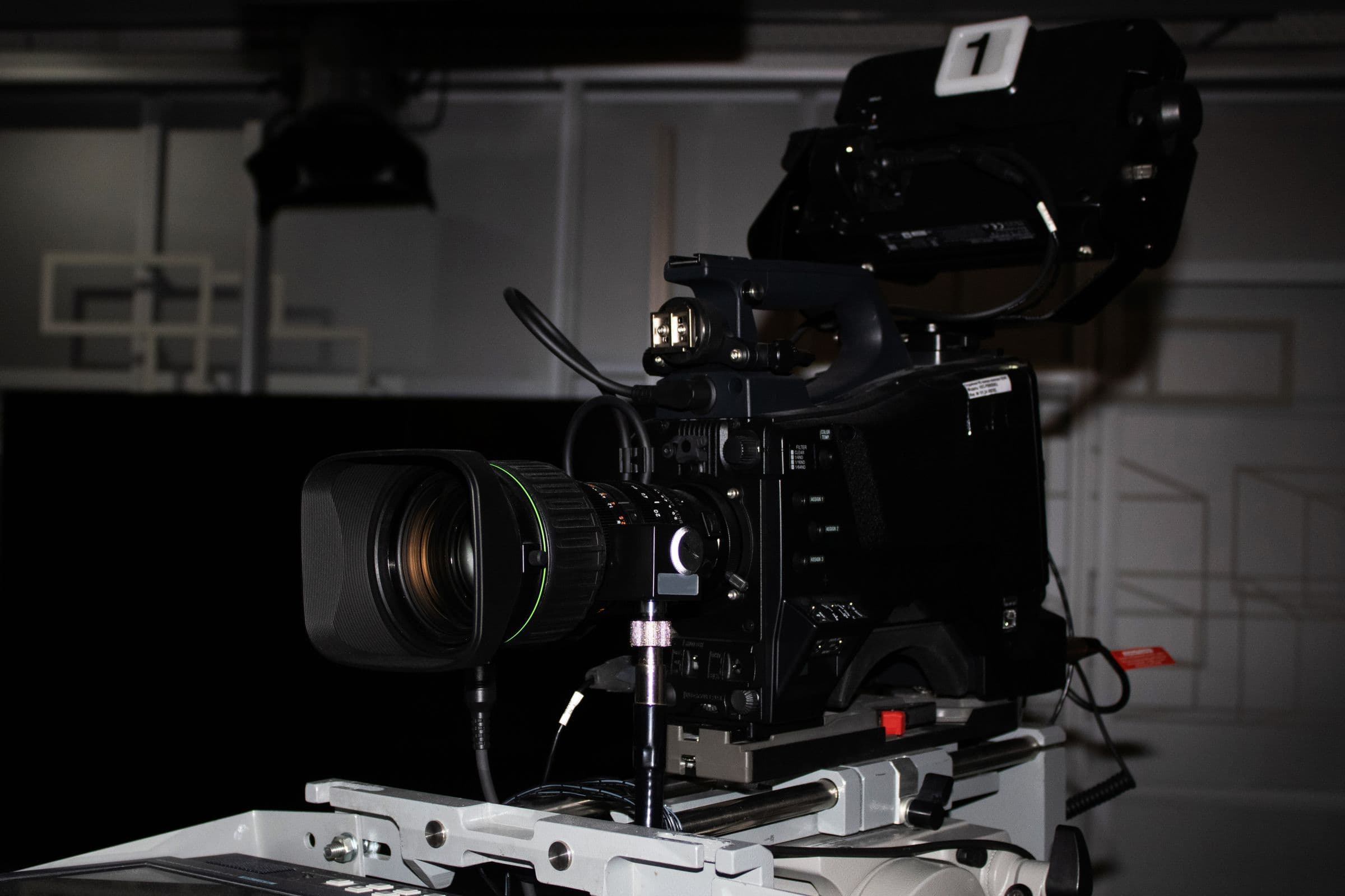 A studio cinema camera on its pedestal, lit low in a blacked-out stage.